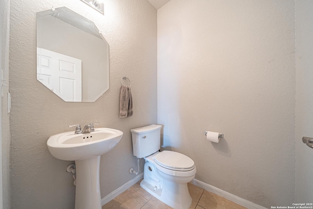 half bathroom with baseboards, toilet, and tile patterned floors