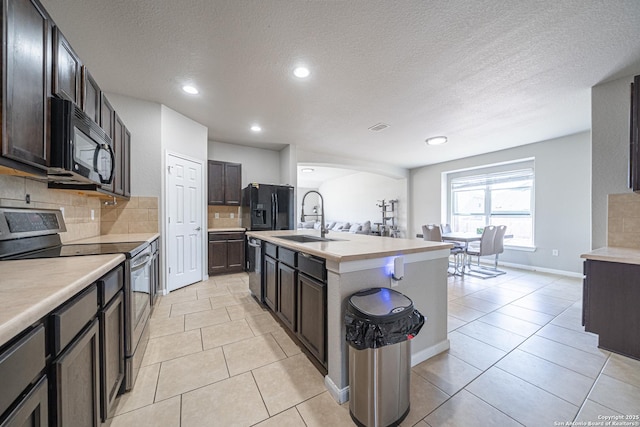 kitchen with light tile patterned flooring, a sink, light countertops, black appliances, and tasteful backsplash