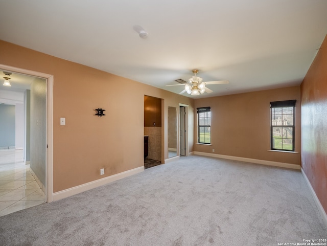 unfurnished room featuring light tile patterned floors, a tile fireplace, light colored carpet, a ceiling fan, and baseboards