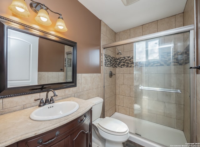 full bathroom with a stall shower, vanity, toilet, and tile walls