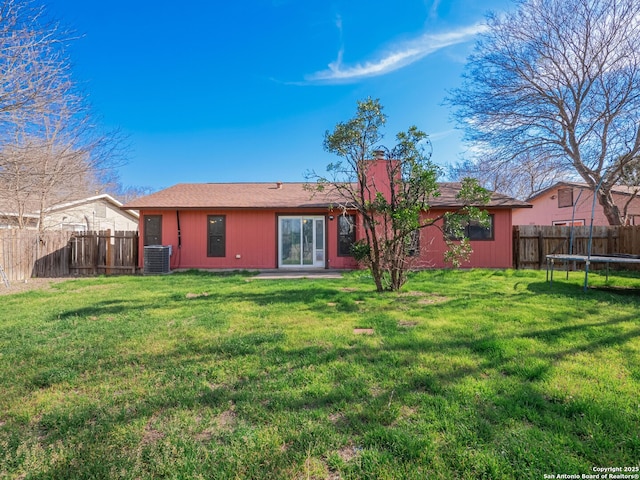 back of property with central AC unit, a lawn, a fenced backyard, a chimney, and a trampoline