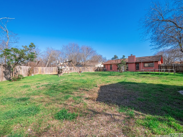 view of yard with a trampoline, a playground, and a fenced backyard