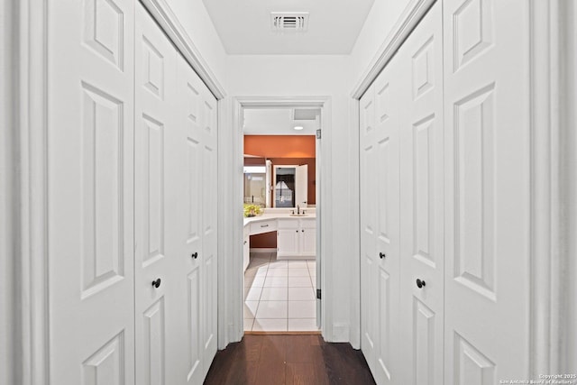 hallway with dark wood finished floors, visible vents, and a sink