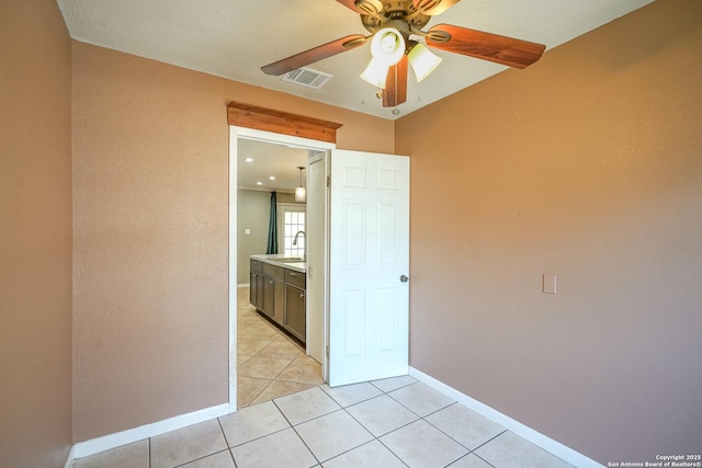 empty room with light tile patterned floors, ceiling fan, a sink, visible vents, and baseboards