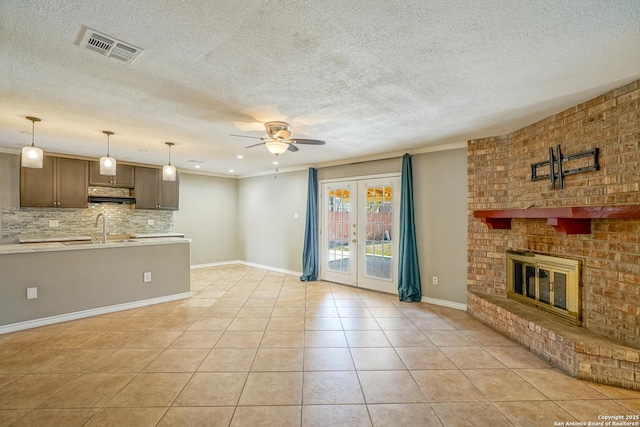 unfurnished living room with light tile patterned floors, ceiling fan, a fireplace, visible vents, and french doors