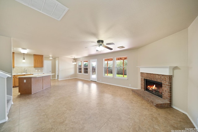 unfurnished living room featuring baseboards, visible vents, ceiling fan, a fireplace, and a sink