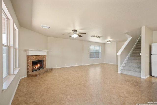 unfurnished living room with visible vents, a fireplace, stairway, and ceiling fan