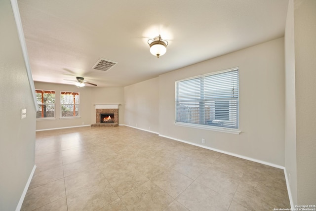 unfurnished living room with a brick fireplace, baseboards, visible vents, and a ceiling fan