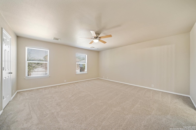 spare room featuring light colored carpet, visible vents, ceiling fan, a textured ceiling, and baseboards