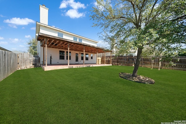 back of property with a chimney, a patio area, a yard, and a fenced backyard