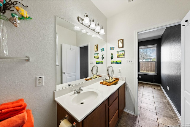 bathroom featuring a textured wall, tile patterned floors, vanity, and baseboards