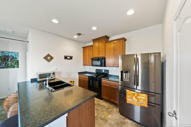 kitchen with visible vents, brown cabinetry, dark countertops, black appliances, and a sink