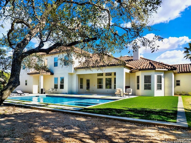 rear view of house featuring a tiled roof, a patio area, a lawn, and a chimney