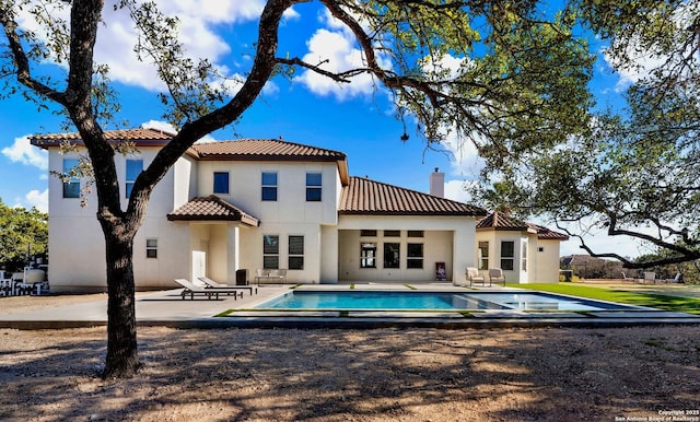 back of property with an outdoor pool, a chimney, a tiled roof, a patio area, and stucco siding