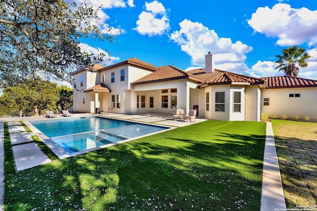 rear view of property featuring a tile roof, a patio, a chimney, stucco siding, and a lawn