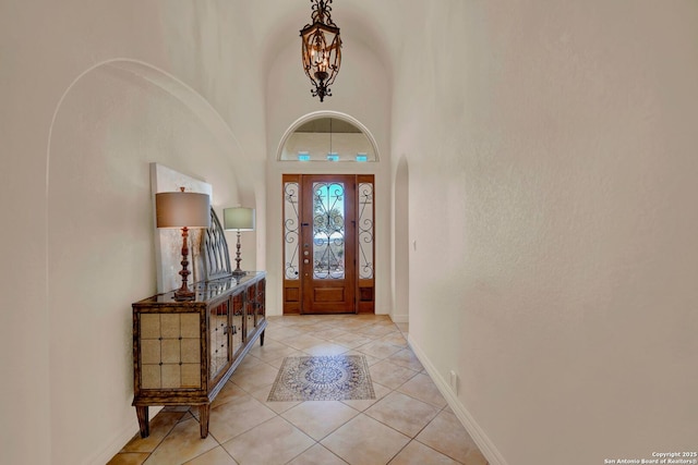 foyer entrance with a chandelier, a high ceiling, light tile patterned flooring, and baseboards