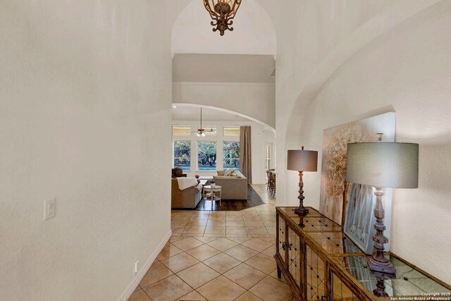 corridor with a towering ceiling, baseboards, arched walkways, and light tile patterned flooring