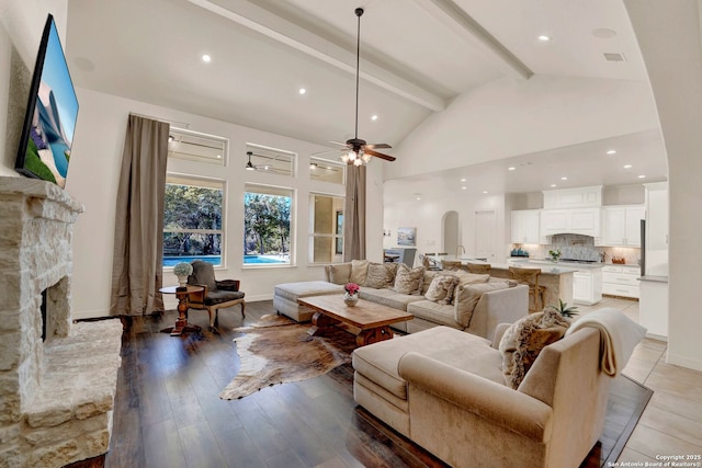 living area featuring arched walkways, light wood-type flooring, a fireplace, high vaulted ceiling, and beam ceiling