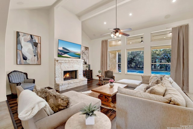 living room featuring baseboards, beamed ceiling, wood finished floors, a stone fireplace, and high vaulted ceiling