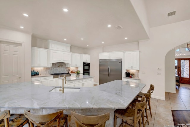 kitchen featuring arched walkways, light tile patterned floors, a spacious island, appliances with stainless steel finishes, and a sink