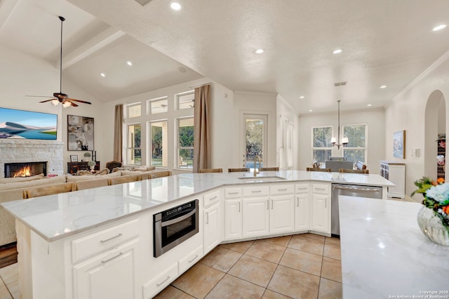 kitchen featuring light stone countertops, a stone fireplace, stainless steel dishwasher, a sink, and light tile patterned flooring