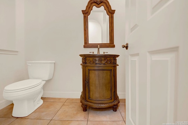 half bathroom featuring toilet, tile patterned flooring, baseboards, and vanity