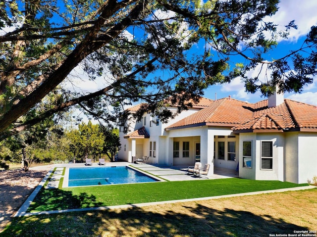 rear view of house featuring a patio area, a lawn, a tiled roof, and stucco siding