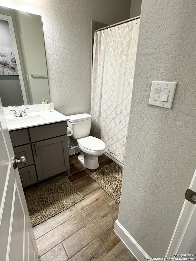 bathroom with curtained shower, a textured wall, toilet, vanity, and wood finished floors