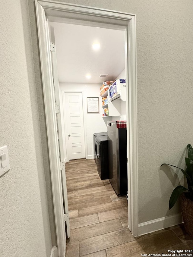 clothes washing area with laundry area, baseboards, washer and clothes dryer, and wood finished floors