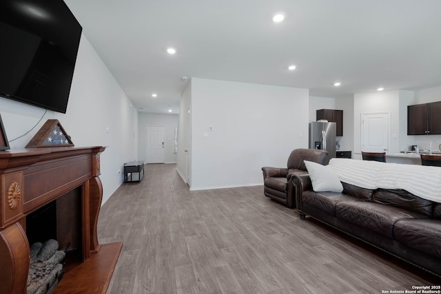 living area featuring recessed lighting, light wood-type flooring, and a fireplace with raised hearth