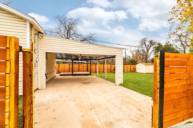 view of patio with an outbuilding, concrete driveway, a storage shed, fence, and a carport