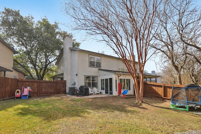 back of property featuring a yard, a trampoline, a chimney, and a fenced backyard