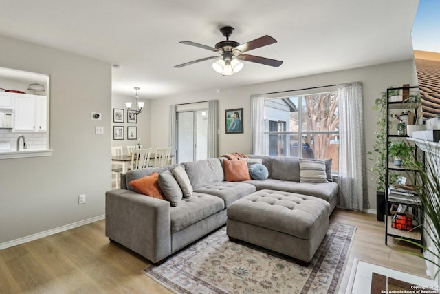 living room with baseboards, light wood finished floors, and ceiling fan with notable chandelier