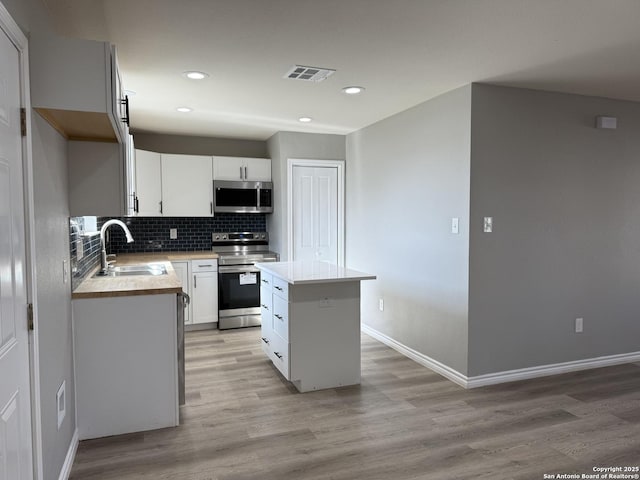 kitchen featuring visible vents, backsplash, appliances with stainless steel finishes, a sink, and a kitchen island