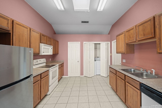 kitchen featuring washer and clothes dryer, visible vents, a sink, vaulted ceiling with skylight, and white appliances