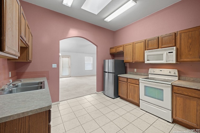 kitchen featuring light carpet, white appliances, arched walkways, brown cabinetry, and a sink