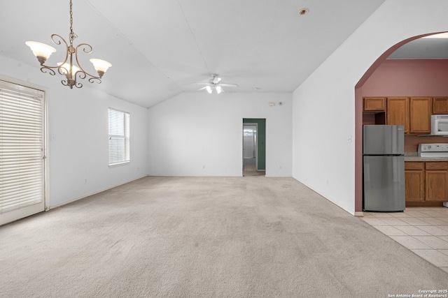 unfurnished living room featuring ceiling fan with notable chandelier, arched walkways, vaulted ceiling, and light colored carpet