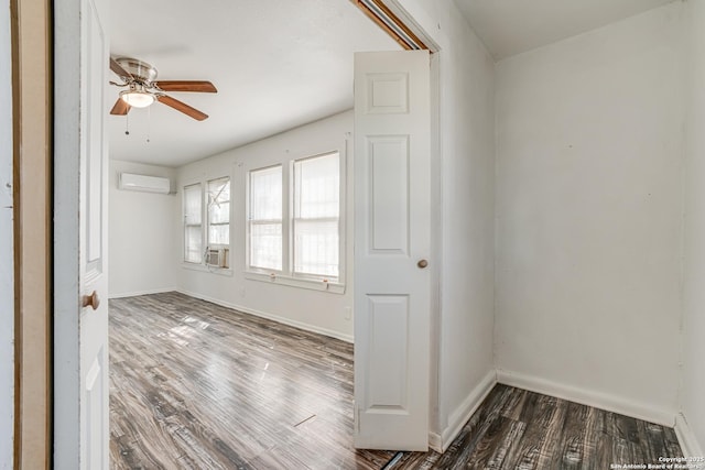 empty room featuring dark wood-style floors, a wall unit AC, and baseboards