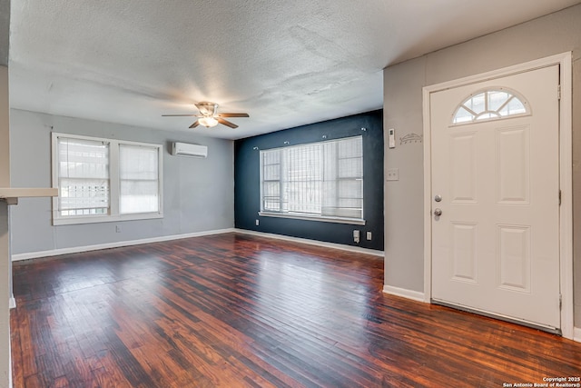 entrance foyer featuring baseboards, a ceiling fan, wood finished floors, a textured ceiling, and an AC wall unit