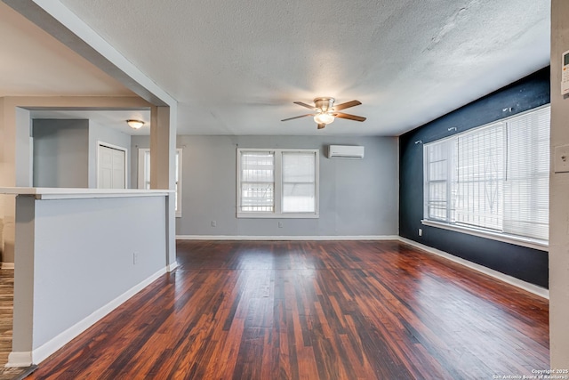 unfurnished room featuring a textured ceiling, a wall unit AC, wood finished floors, and baseboards