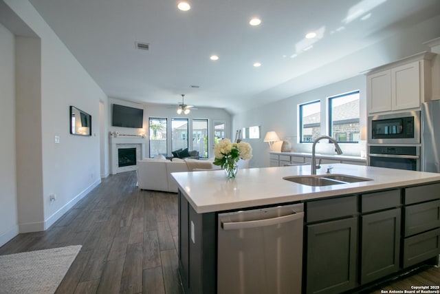 kitchen with stainless steel appliances, a fireplace, a sink, light countertops, and an island with sink