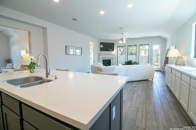 kitchen with visible vents, open floor plan, wood finish floors, a fireplace, and a sink