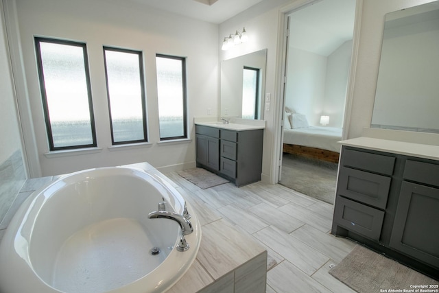 ensuite bathroom featuring baseboards, vanity, a bath, and connected bathroom