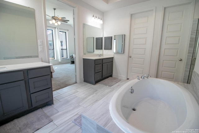 bathroom with baseboards, ceiling fan, two vanities, a garden tub, and a sink