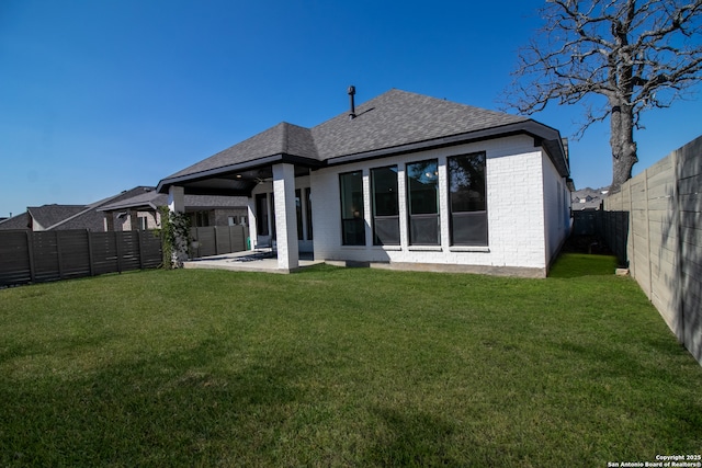 rear view of house with roof with shingles, brick siding, a lawn, and a fenced backyard