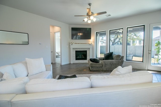 living area with wood finished floors, visible vents, baseboards, a ceiling fan, and a glass covered fireplace