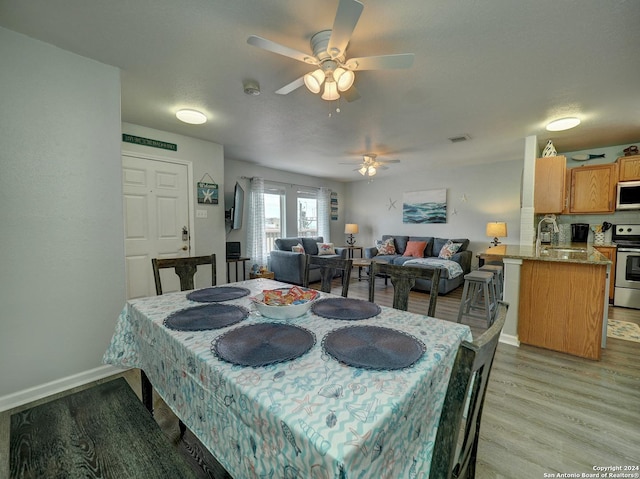 dining area featuring a ceiling fan, baseboards, visible vents, and light wood finished floors