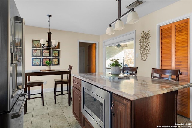 kitchen with light tile patterned floors, visible vents, appliances with stainless steel finishes, light stone counters, and hanging light fixtures