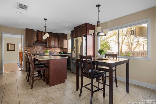 kitchen featuring visible vents, decorative backsplash, a kitchen island, stainless steel appliances, and wall chimney range hood