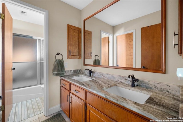 bathroom featuring double vanity, bath / shower combo with glass door, a sink, and visible vents